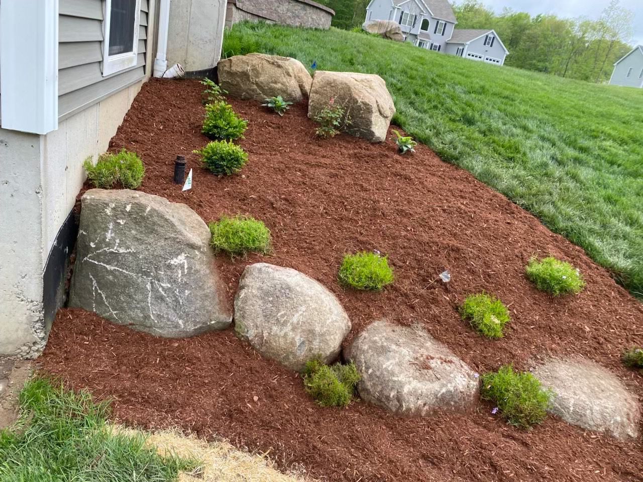 Boulders and shrubs set into a mulched slope beside a house